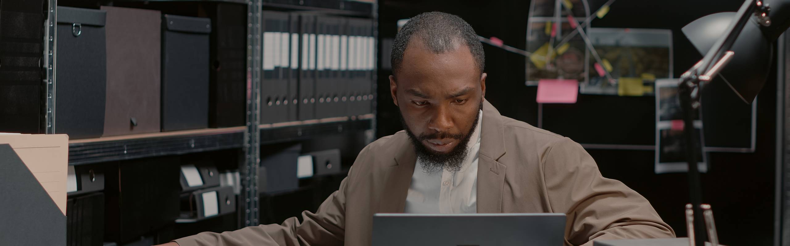Police officer putting crime case photo on wall board, analyzing clues and forensic evidence to catch suspect. African american agent looking at files and statements, detective map.